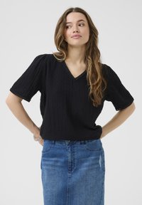 Haut noir à manches courtes avec un motif texturé, décolleté en V et bordure festonnée, associé à une jupe en denim bleu.