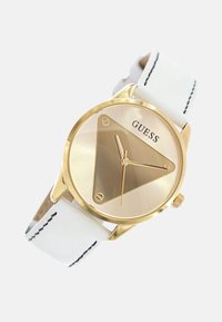 Gouden horloge met een driehoekige wijzerplaat, witte leren band en zwarte stiksels. Beschikt over minimalistische uurmarkeringen en logo.
