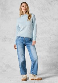 Ljust blå ribbad tröja med långa ärmar, parat med blekta blå raka jeans och beige höga sneakers. Strukturerat tyg och avslappnad passform.