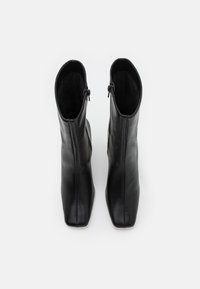Botas de cuero negro hasta el tobillo con punta cuadrada, cierres de cremallera a los lados y una textura suave. Diseñadas para una silueta ajustada.