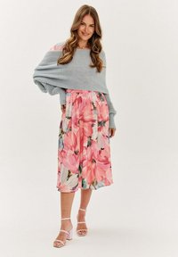 Šaty s kvetinovým vzorom po kolená, s ružovými a modrými vzormi, doplnené svetlosivým pleteným bolerom. Model má na sebe ružové sandále na blokovom podpätku s remienkami.