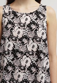 Top senza maniche floreale con sfondo nero e fiori rosa chiaro e bianchi. Il tessuto ha una superficie liscia.