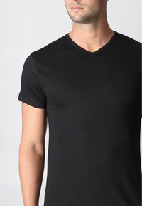 Maglietta nera a maniche corte con scollo a V, realizzata in tessuto morbido, caratterizzata da un design aderente e da cuciture curve sottili.