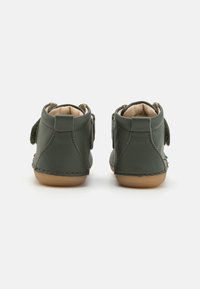 Bottines en cuir vert avec une texture douce, dotées d'une sangle en velcro et d'une semelle en caoutchouc beige. Détails cousus sur les bords.