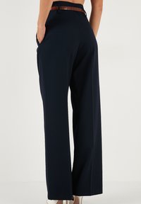 Pantaloni navy cu talie înaltă și picioare largi, dintr-un material fin, cu buzunare laterale și un brâu cu textură de crocodil maro care evidențiază talia.