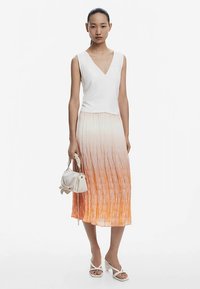 Top alb fără mâneci cu decolteu în V, asortat cu o fustă lungă plisată, care trece de la alb la portocaliu. Accesorizat cu o geantă mică albă și sandale.