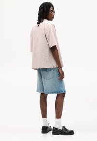 Kortærmet, lyserød tekstureret skjorte; blå denimshorts; hvide sokker; sorte sko med dekorative hardware; set fra bagen.
