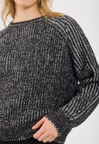 Knautsīts džemperis melnbālā krāsā ar ribotu apkakli un aprocēm, ar teksturētu, slāņotu rakstu visā virsmas platībā.