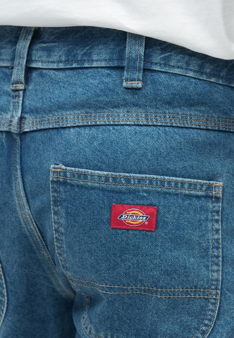 Blue denim shorts with a red and yellow Dickies logo patch on the back pocket. Features visible stitching and a classic cut.