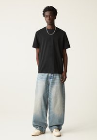 Sort bomulds T-shirt med rund hals, parret med løse blå denimjeans, der har en falmet finish og en lige benstil.