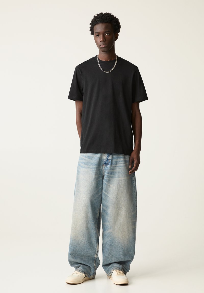 Sort bomulds T-shirt med rund hals, parret med løse blå denimjeans, der har en falmet finish og en lige benstil.