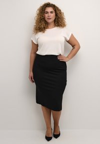 Valkoinen lyhythihainen paita yhdistettynä mustaan kynähameeseen. Kangas on sileä, ja hame on slim fit -mallinen, ulottuen polven alapuolelle.