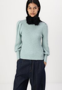 Light blue ribbed knit sweater with puffed shoulders and a black faux fur collar. Paired with dark denim high-waisted trousers.