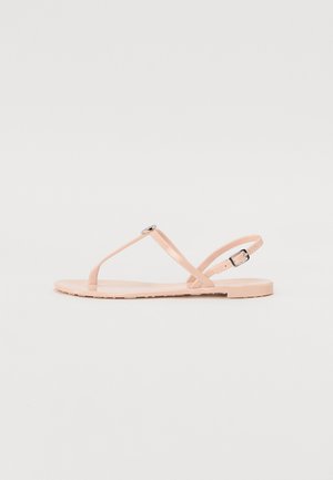 Lys rosa flate sandaler med tynne, matte stropper og en spenne detalj. Flat såle med et teksturert mønster for godt grep.