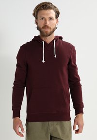 Bordeaux hoodie gemaakt van zacht materiaal, met een voorzak, witte trekkoorden en geribbelde manchetten voor een comfortabele pasvorm.