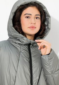 Giacca a vento grigia con cappuccio, con texture lucida, dotata di zip frontale, design trapuntato e cordino regolabile nel cappuccio.