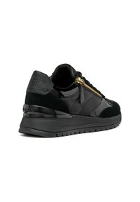 Zapatilla negra con acentos de charol y gamuza, que presenta un talón texturizado, detalle de cremallera dorada y una suela de goma gruesa.