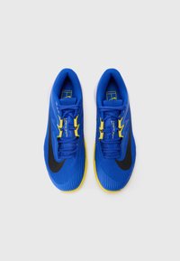 Blå atletiske sko med et teksturert stoffoverdel, gule detaljer, svart Nike-svush og en buet gul såle. Snøring øverst.