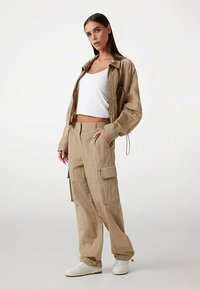 Chaqueta beige con un corte holgado, top blanco corto y pantalones cargo a juego con bolsillos, combinados con zapatillas blancas.