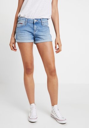 Shorts en denim bleu clair avec des ourlets roulés, design traditionnel à cinq poches et fermeture à bouton à l'avant. Portés avec des baskets blanches.