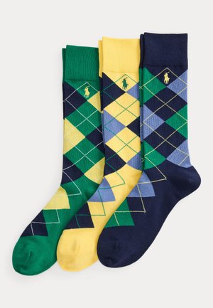 Drei Paar argylegemusterte Socken in Grün, Gelb und Marineblau, jeweils mit einem kleinen gestickten Logo nahe der Bündchen.