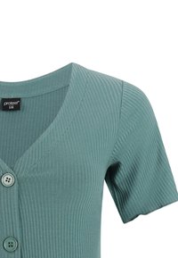 Petrolejový žebrovaný krátky kardigán s výstrihom do V a dvoma prednými gombíkmi, veľkostná etiketa „protest S36“ vo vnútri goliera.