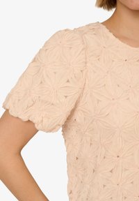 Top corto a maniche corte di colore rosa chiaro con un motivo floreale testurizzato, scollatura e orlo a onda, realizzato in un tessuto morbido e leggero.
