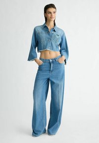 Giacca di jeans cropped azzurro chiaro con maniche svasate e tasca a patch testurizzata, abbinata a jeans in denim azzurro chiaro a gamba larga.