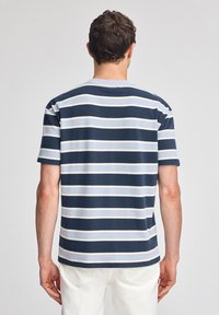 Marinblå och ljusblå randig t-shirt, kort ärm, avslappnad passform, bomullsmaterial, rundad halsringning, synliga sömdetaljer på baksidan.