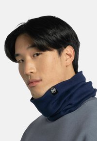 Gaiter de cuello de punto en color marino con un acabado texturizado y parche de logo, llevado ceñido alrededor del cuello, combinado con una sudadera gris.