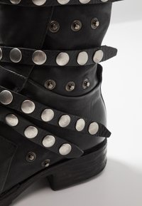 Czarne skórzane buty z metalowymi ćwiekami i paskami. Posiadają teksturowaną powierzchnię oraz niski, warstwowy obcas. Akcenty z srebrnego metalu.