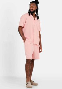 Set di pigiama in morbido tessuto rosa chiaro. Camicia con bottoni a maniche corte e taschino abbinata a pantaloni corti. Vestibilità comoda, design minimale.