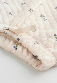 Tessuto trapuntato in morbido rosa, con piccoli fiori ricamati in blu e verde. Chiuso con un nastro di stoffa beige.