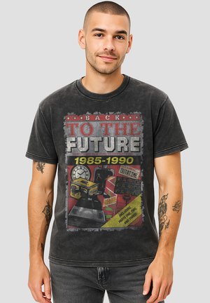 Young man with short hair wearing a black "Back to the Future 1985-1990" graphic T-shirt with colorful movie-themed images.