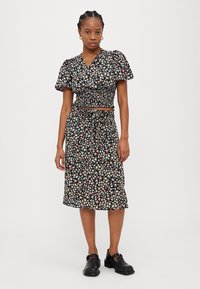 Abito con stampa floreale caratterizzato da uno sfondo nero con piccoli fiori multicolori, maniche a sbuffo corte e vita aderente con dettaglio a fiocco.