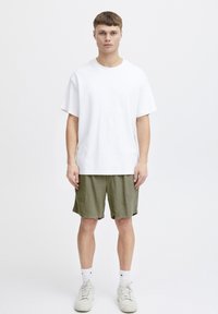 T-shirt en coton blanc à manches courtes, associé à un short en olive texturé, complété par des baskets blanches et des chaussettes blanches mi-mollet.