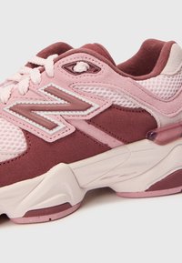 Chaussures de sport rose et bourgogne en matériaux en maille et en suède. Dotées d'une semelle épaisse et d'un logo "N" bien visible sur le côté. Accents texturés visibles.