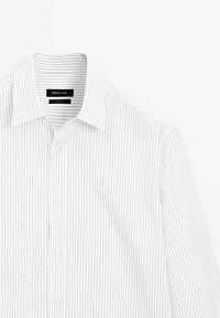 Chemise blanche à boutons avec fines rayures verticales noires, col et boutonnage sur le devant. Le tissu est lisse avec une légère brillance, mettant en valeur des coutures soignées.
