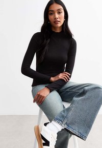 Svart ribbad långärmad topp med scallopkant, matchad med ljusblå vida jeans och vita sneakers med svarta detaljer.