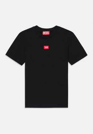 T-shirt noir à manches courtes en coton, avec un petit patch rectangulaire rouge sur la poitrine comportant du texte blanc.