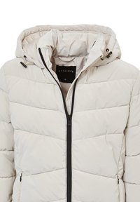 Beige gesteppte Pufferjacke mit Kapuze, schwarzem Reißverschluss, Kordelzügen und einem Etikett mit der Aufschrift "CALLIOPE S" im Kragen.