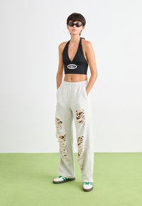 Musthave musta halter-top, mille on logo, koos heledate hallide dressipükstega, millel on suured kulunud lõikude detailid. Mudel kannab musti prille ja roheliste detailidega jalanõusid.