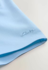 Himmelblauer Stoff mit glatter Textur, versehen mit einem abgerundeten Saum und einem gestickten "Clarks"-Logo in der unteren Ecke.