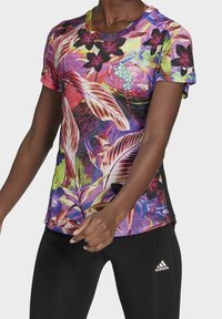 Sportovní tričko s krátkým rukávem, které má barevný květinový vzor v odstínech fialové, růžové a zelené, vyrobené z lehkého materiálu.