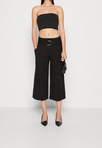 Svart bandeau-topp kombinerad med svarta vida cropped-byxor som har ett bälte med en cirkulär silverfärgade spänne och fickor. Svarta spetsiga klackar.