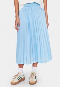 Vaaleansininen laskostettu hame, joka on valmistettu tasaisesta kankaasta. Hameessa on vyötäröosa, ja se ulottuu polven keskikohtaan. Yhdistettynä valkoisiin sukkiin ja rentoihin tennareihin.