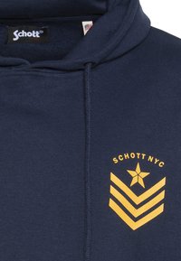 Granatowa bluza z kapturem wykonana z bawełny, z żółtą gwiazdą i wzorem w jodełkę na przodzie. Bluza posiada kaptur ze sznurkiem oraz metkę wewnątrz.