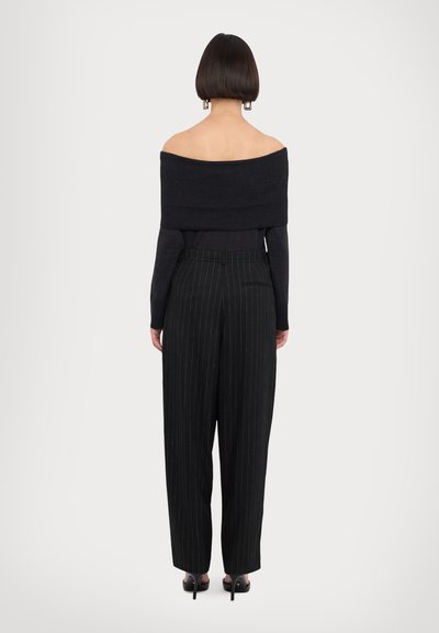 Top noir en tricot dégageant les épaules, associé à un pantalon à rayures verticales taille haute, avec des jambes droites et des poches discrètes.