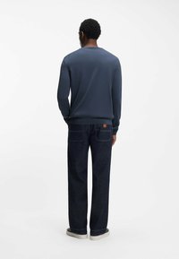 Maglione blu navy a maniche lunghe con polsini e orlo a coste, abbinato a pantaloni di denim scuro con tasche posteriori e design minimalista.
