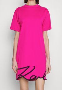 Helles pinkes, übergroßes T-Shirt-Kleid mit kurzen Ärmeln und rundem Ausschnitt. Mit schwarzem, gesticktem "Karl" am Saum. Weiche Textur.